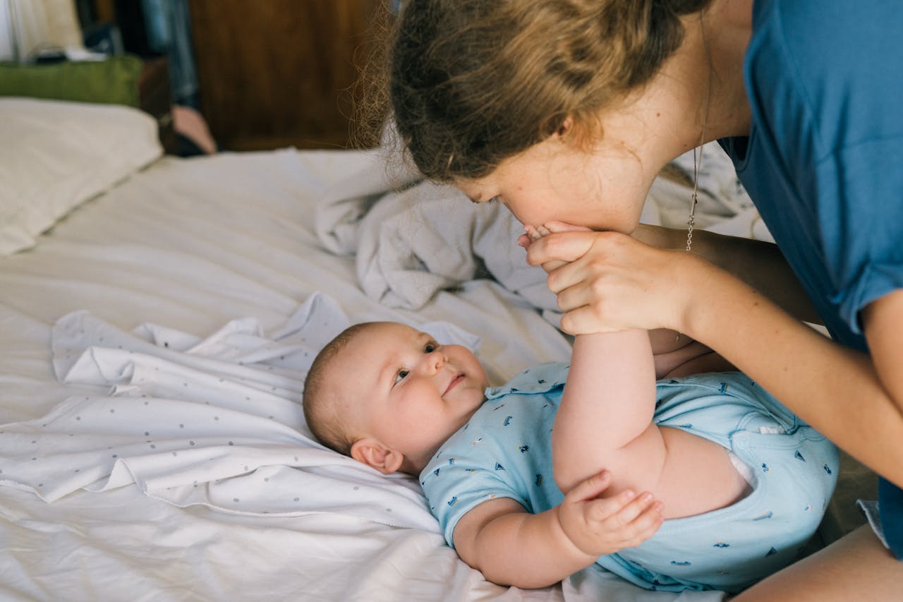 A mother gently kisses her baby's foot on a cozy bed, illustrating love and warmth.