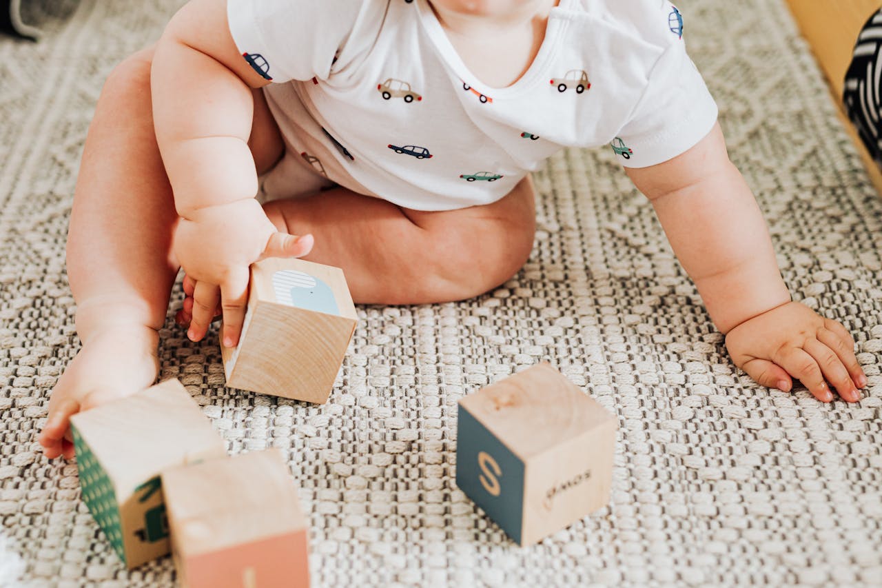 A cute baby plays with colorful wooden blocks on a soft carpet indoors.